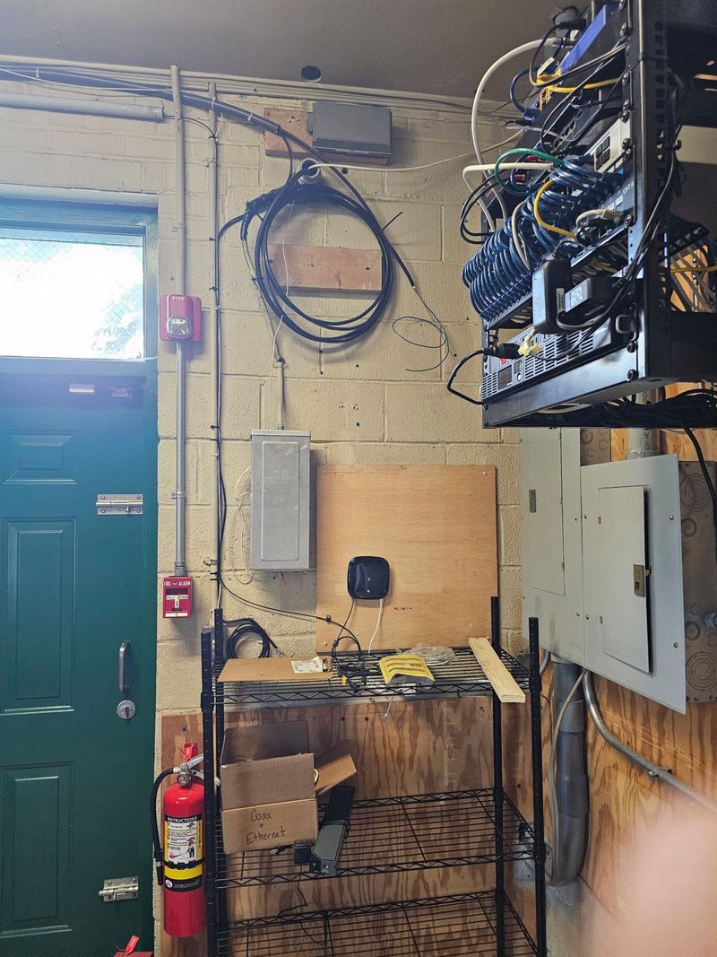 Utility room with wall-mounted network rack, fiber coil and a mesh access point on plywood backboard